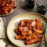 Braised pork ragu with rigatoni in a dish with red wine glasses in the background