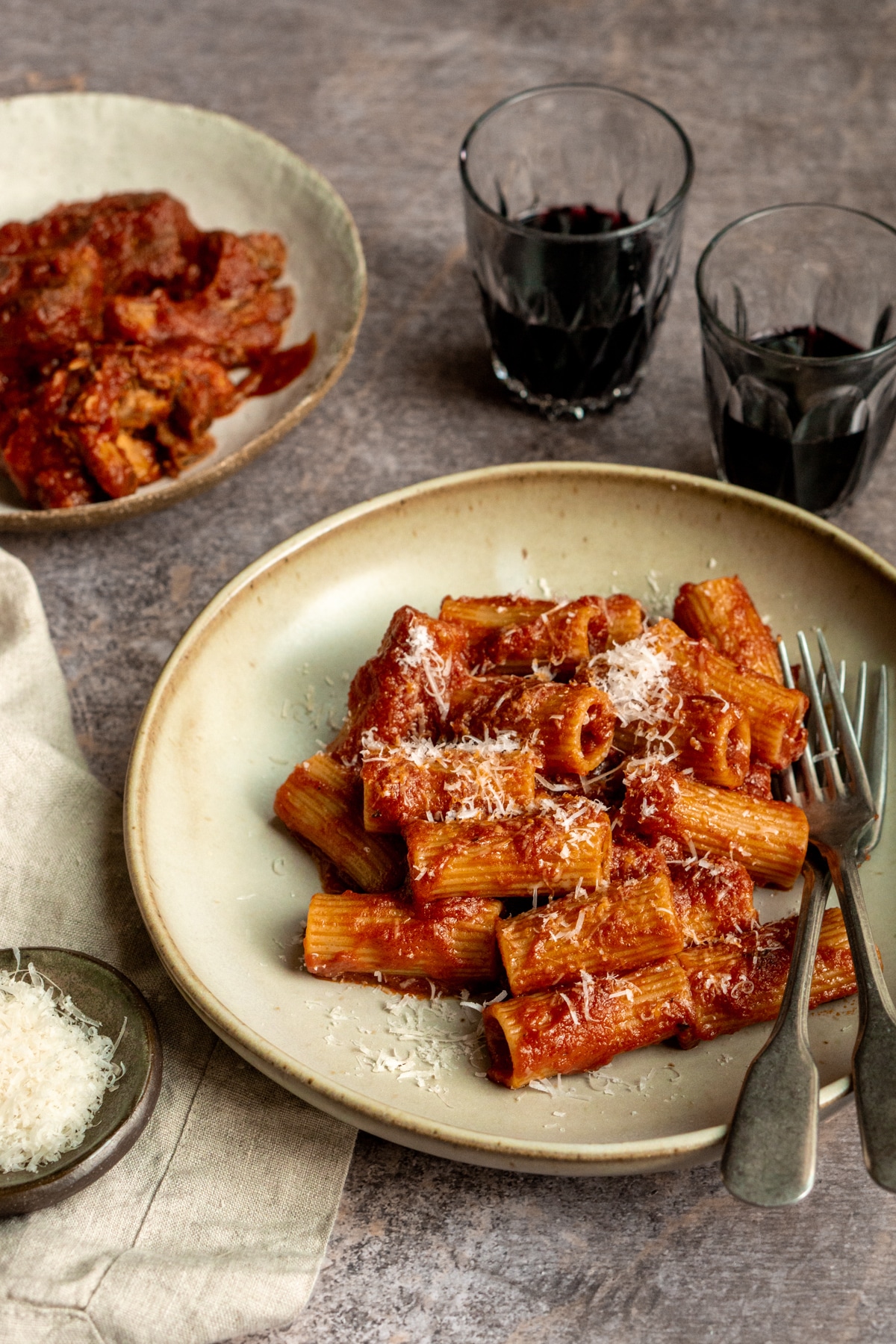 Braised pork ragu with rigatoni in a dish with red wine glasses in the background