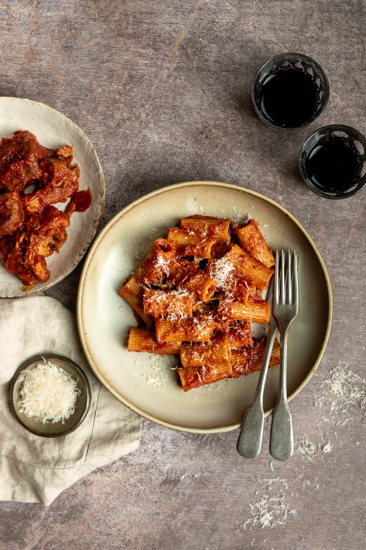 Rigatoni with braised pork ragu sauce in a dish with a small bowl of parmigiano reggiano to the side