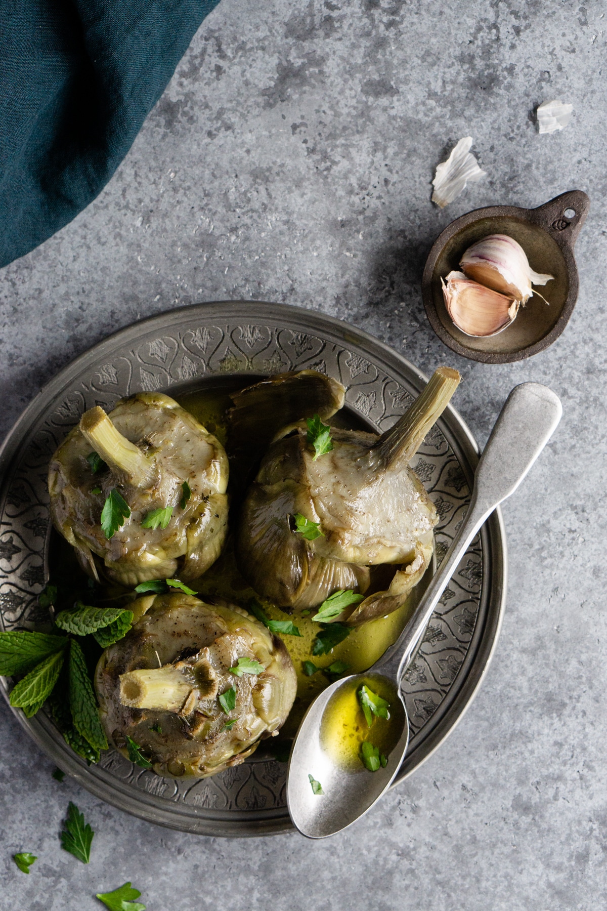 roman artichokes in a plate with a small dish of garlic cloves to the side