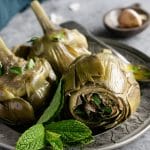 roman artichokes (carciofi alla romana) in a dish with a bunch of mint