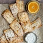 A bunch of chiacchiere on a piece of parchment paper with half an orange to the side