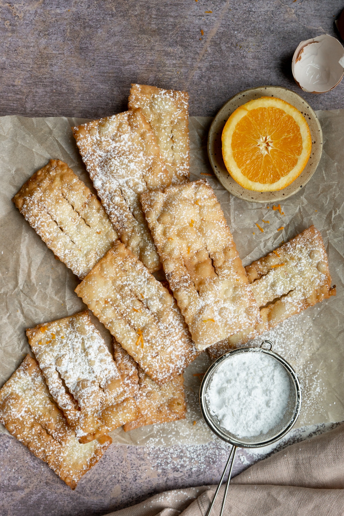 A bunch of chiacchiere on a piece of parchment paper with half an orange to the side