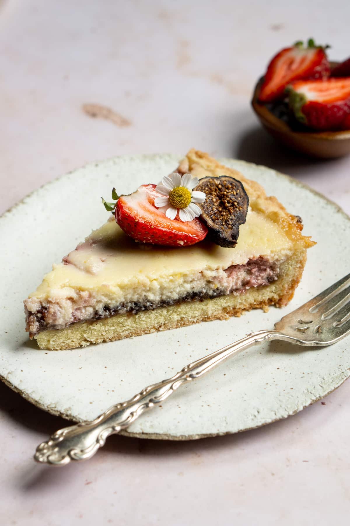 Slice of strawberry ricotta crostata in a plate with fresh strawberries in the background