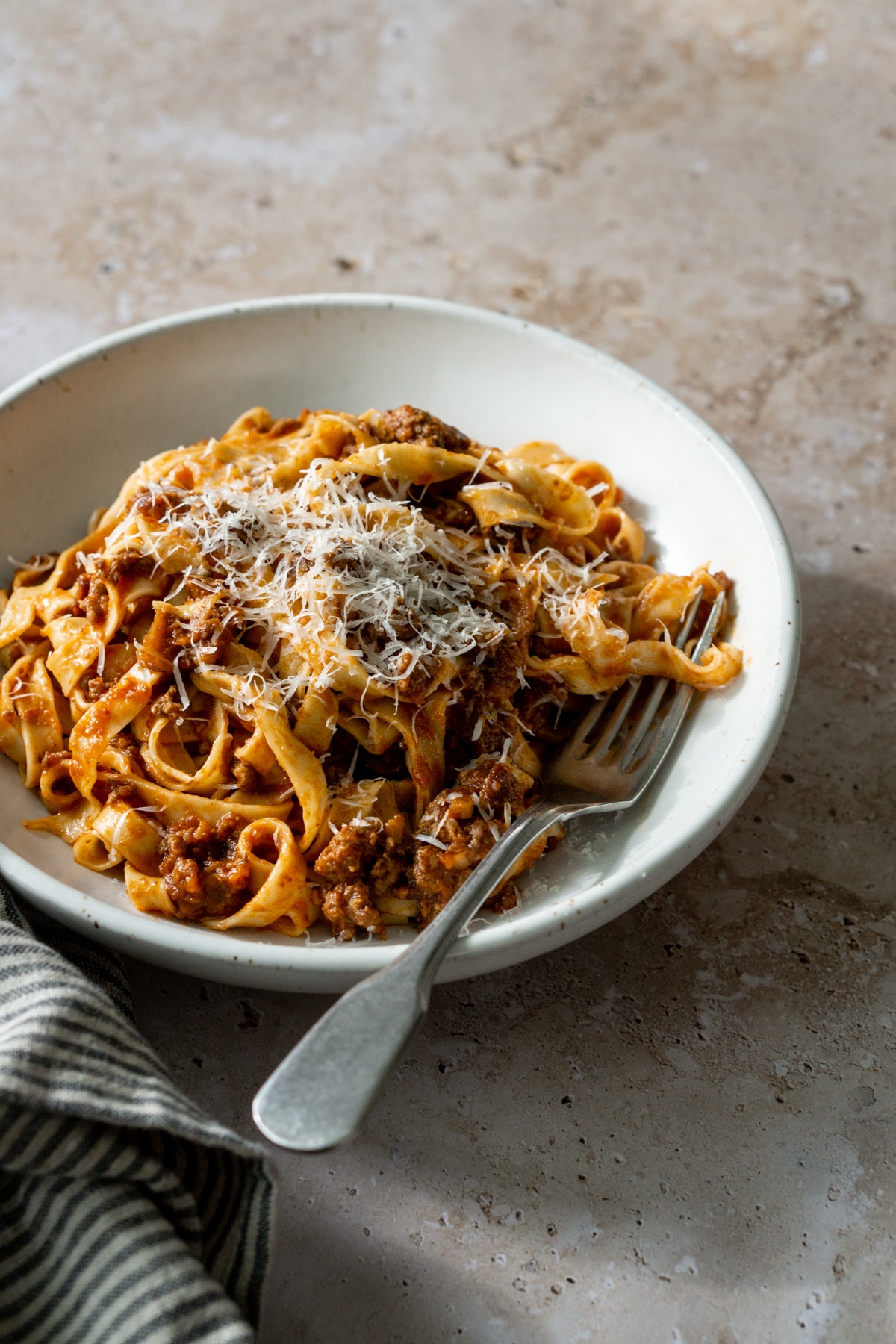 Plate of tagliatelle alla bolognese topped with parmigiano reggiano with a fork