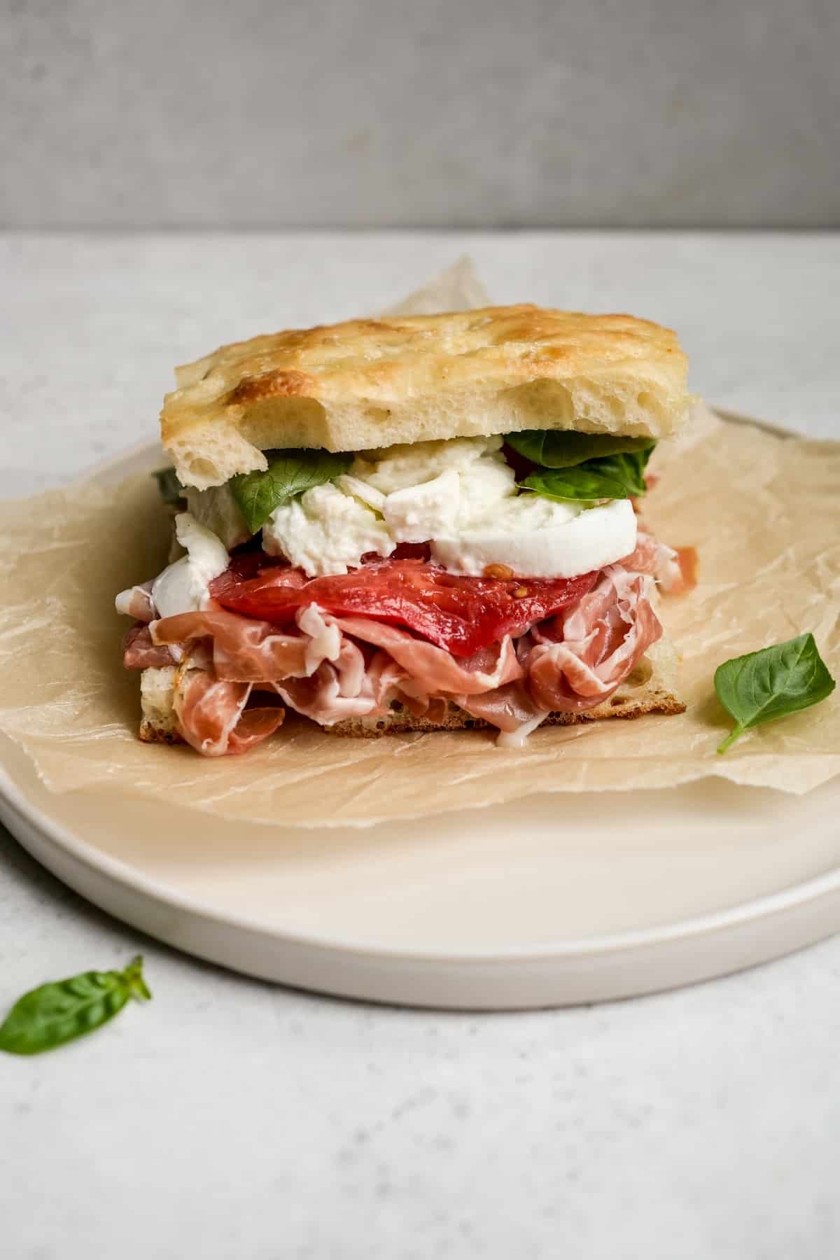 Prosciutto sandwich on a plate with a piece of basil to the side