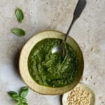 Pesto genovese in a bowl with a small dish of pine nuts to the side
