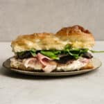 Pancetta sandwich with pecorino cream, sundried tomatoes and arugula on a plate