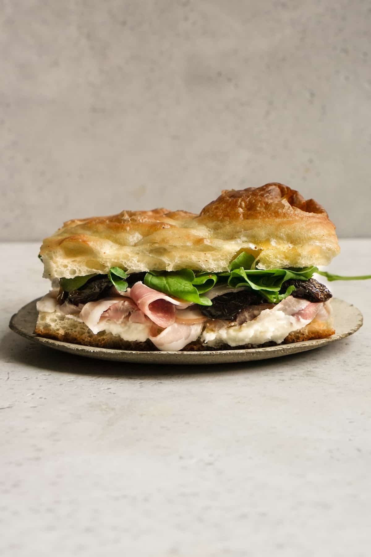 Pancetta sandwich with pecorino cream, sundried tomatoes and arugula on a plate