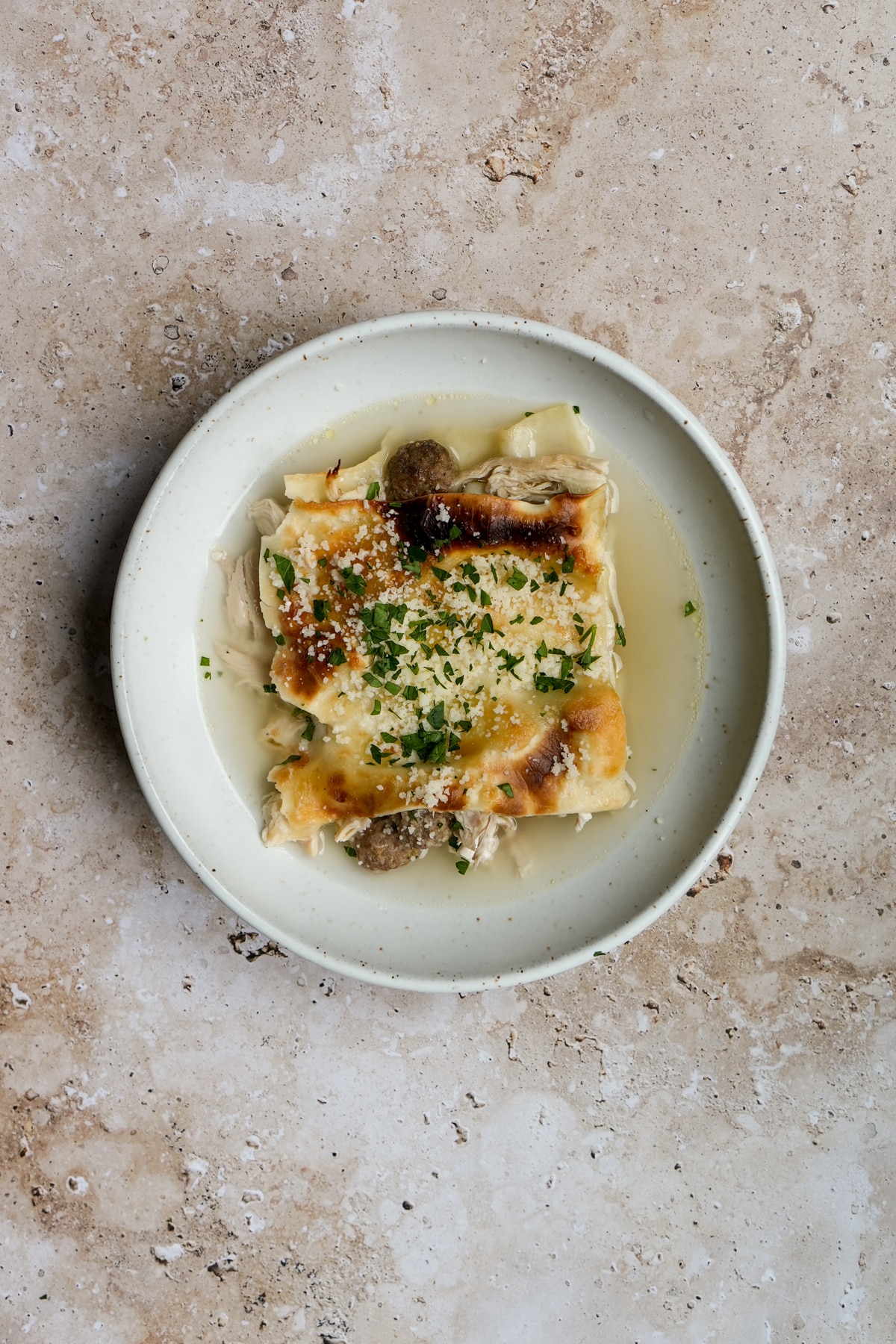 Birds eye view of lasagna in brodo in a plate, surrounded by broth
