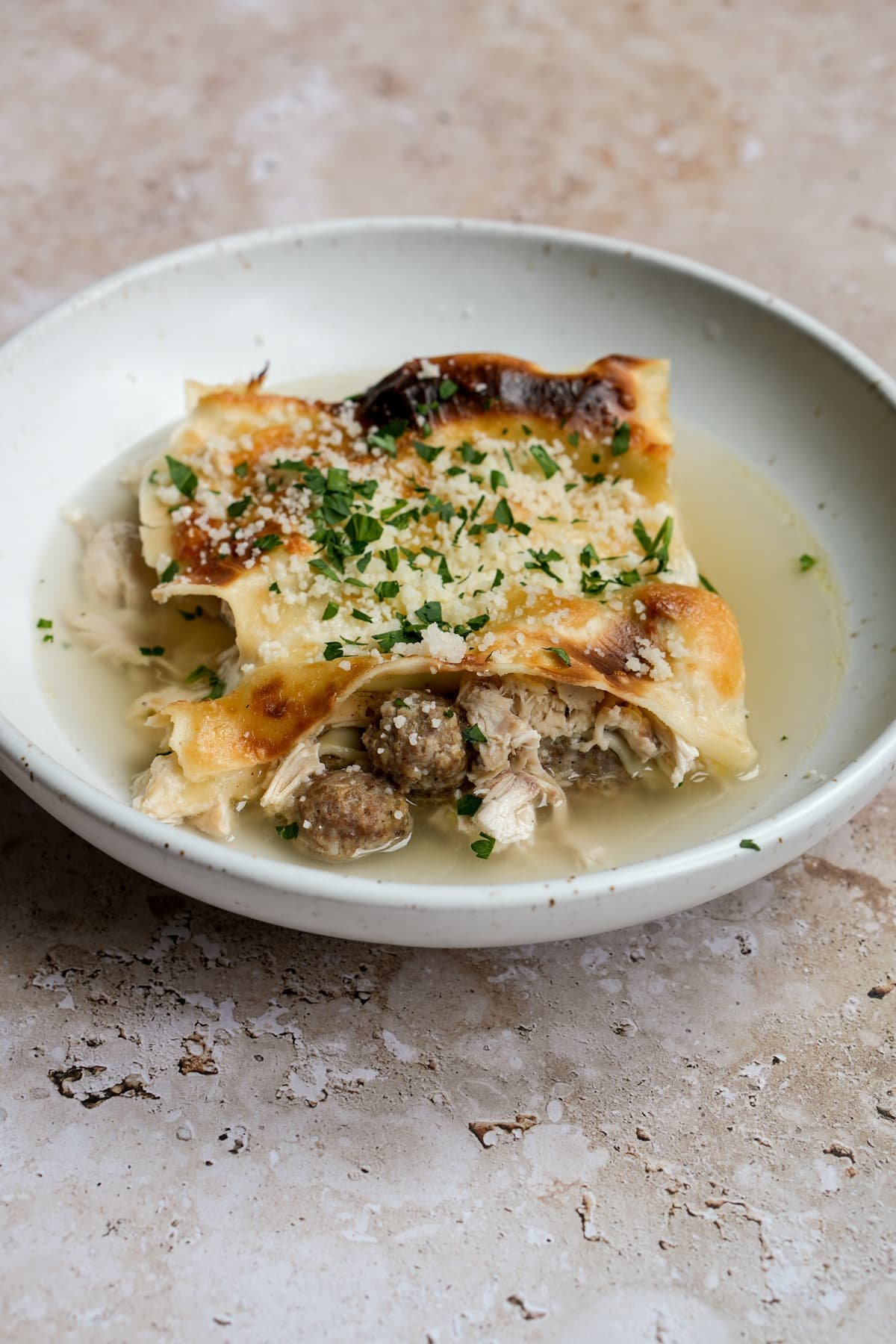 Lasagna in brodo in a plate topped with parmesan and parsley