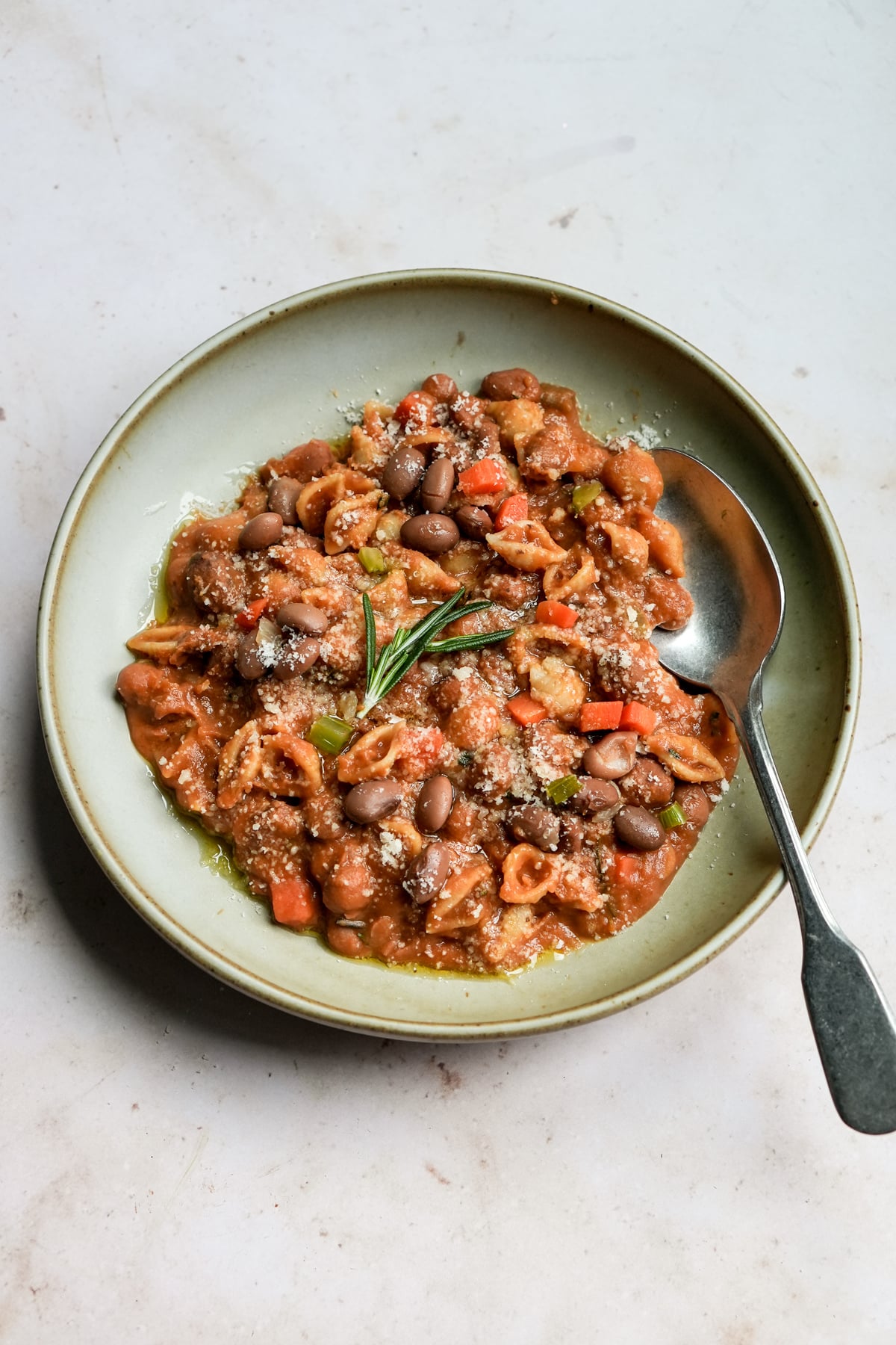 Bowl of pasta fagioli topped with a sprig of rosemary and a spoon to the side