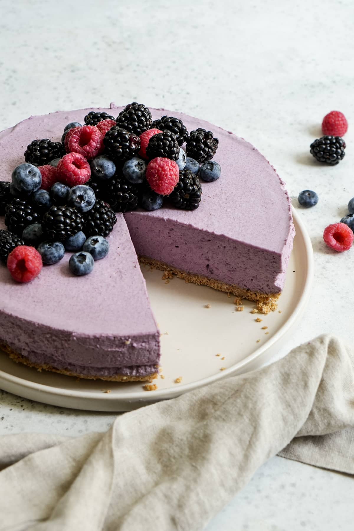 Berry mousse cake topped with fresh berries on a plate with a slice cut out
