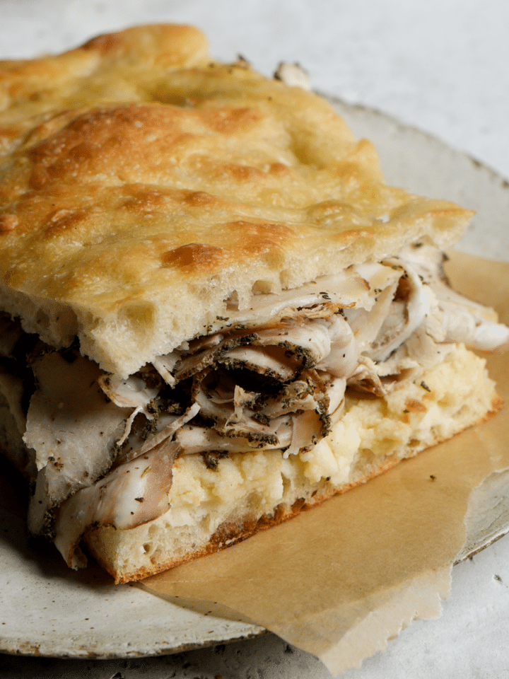 Porchetta sandwich on a piece of parmchment paper, sitting on a plate