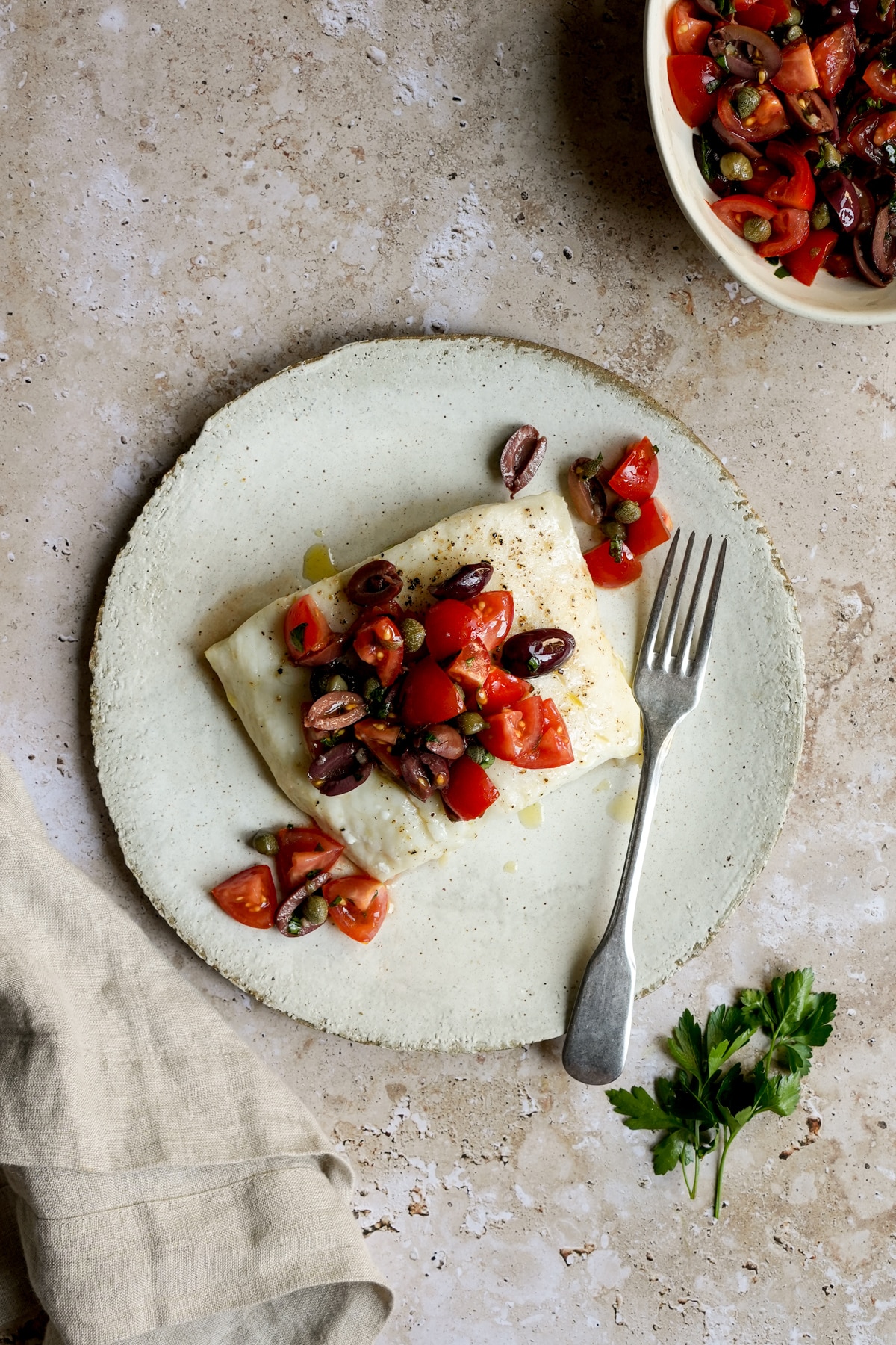Italian halibut with tomatoes, olives and capers in a plate with parsley to the side