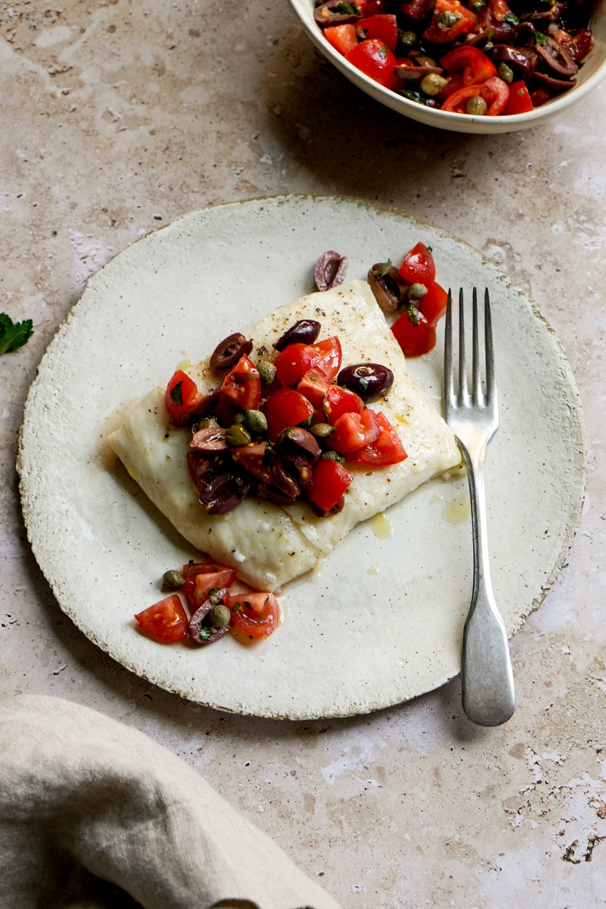Italian halibut with tomatoes, olives and capers in a plate with a fork