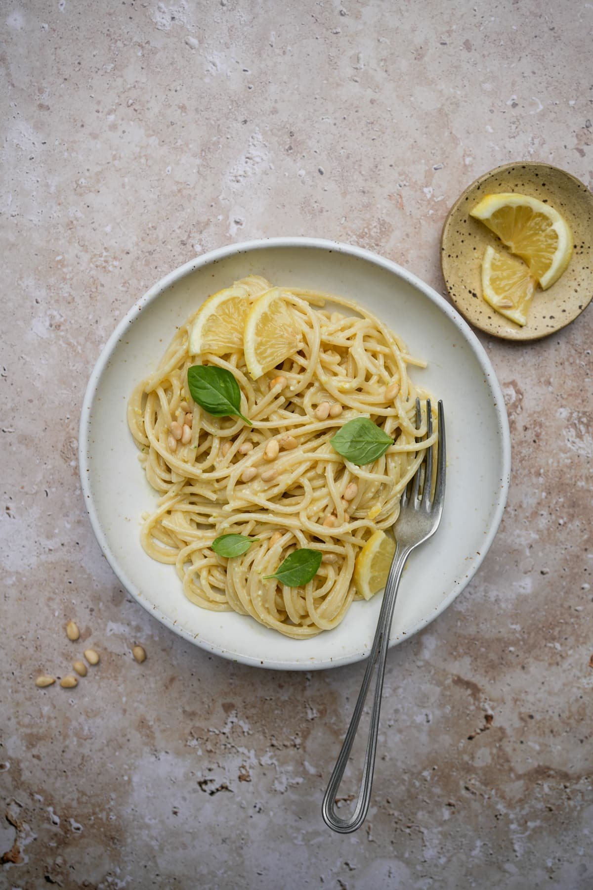 Lemon pesto pasta in a dish topped with pine nuts, fresh basil and lemon