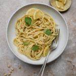 Lemon pesto pasta in a dish topped with fresh basil, lemons, and pine nuts