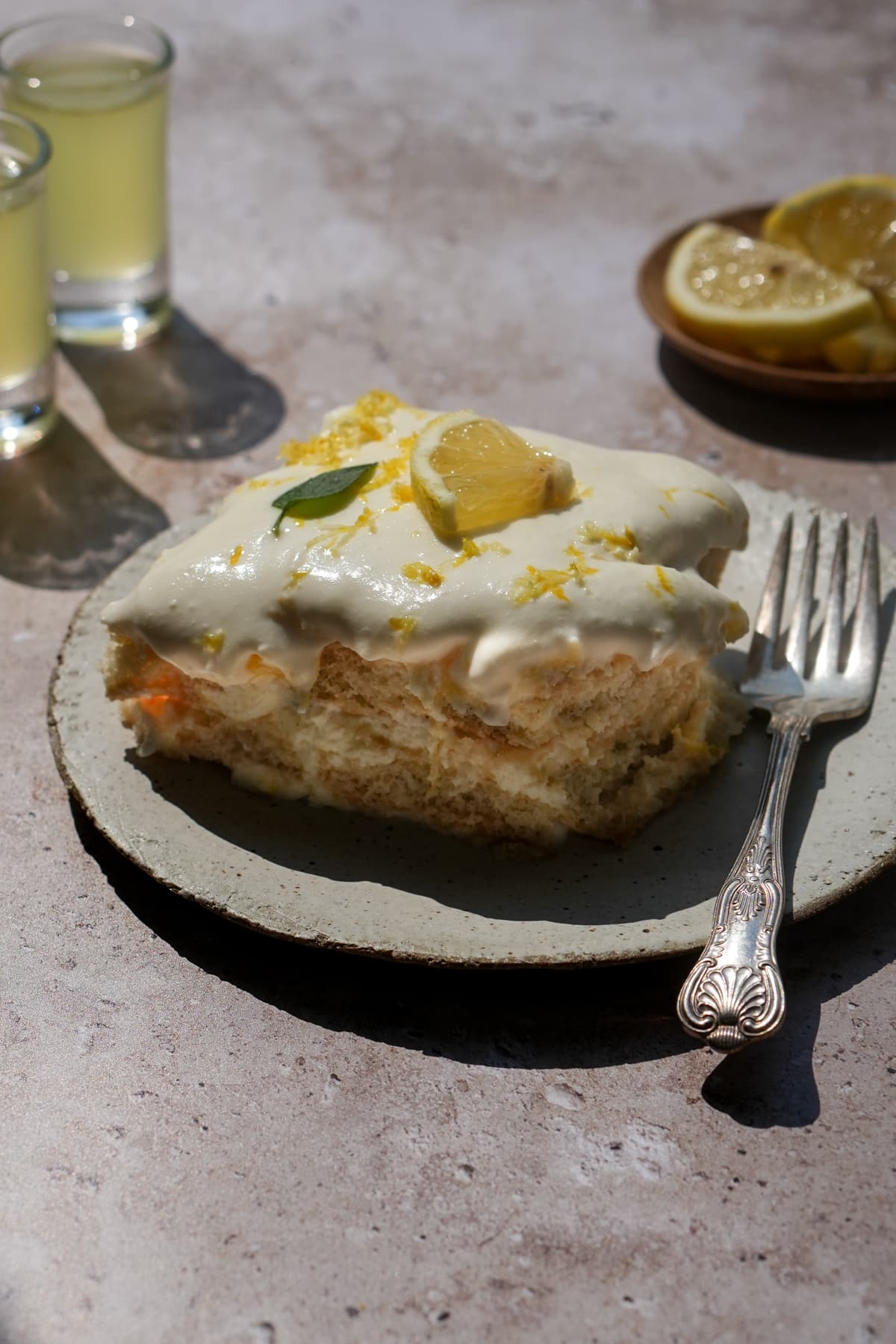 Piece of limoncello tiramisu in a plate with limoncello glasses in the background