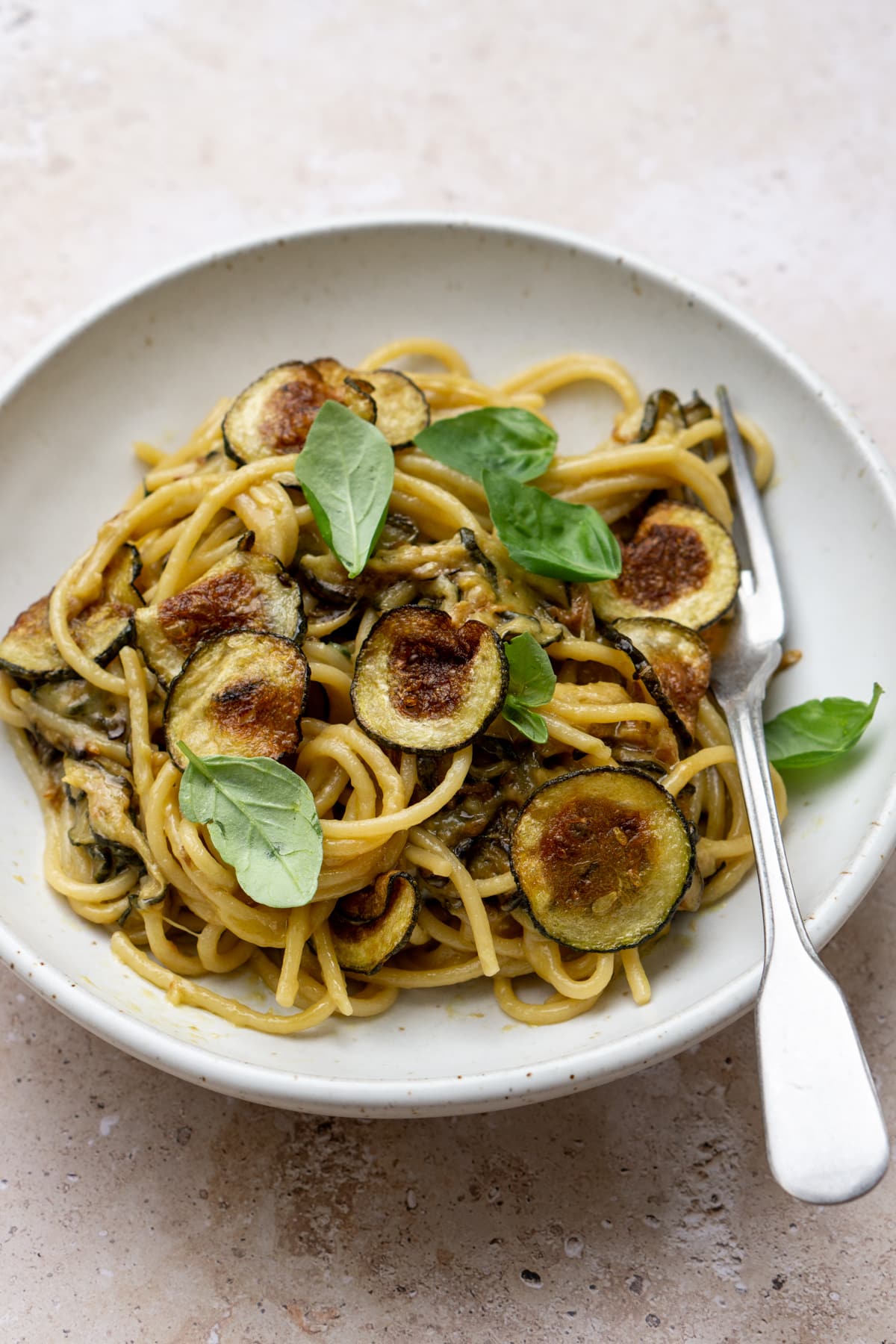 Spaghetti alla nerano in a dish topped with fried zucchini and fresh basil