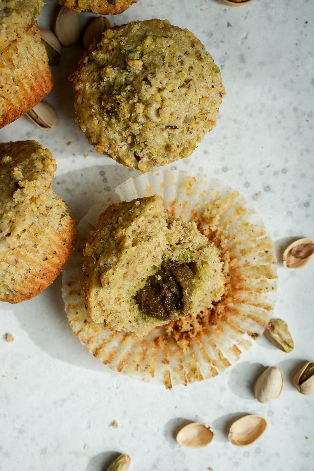 Half of a pistachio muffin with pistachio cream in the middle surrounded by fresh pistachios