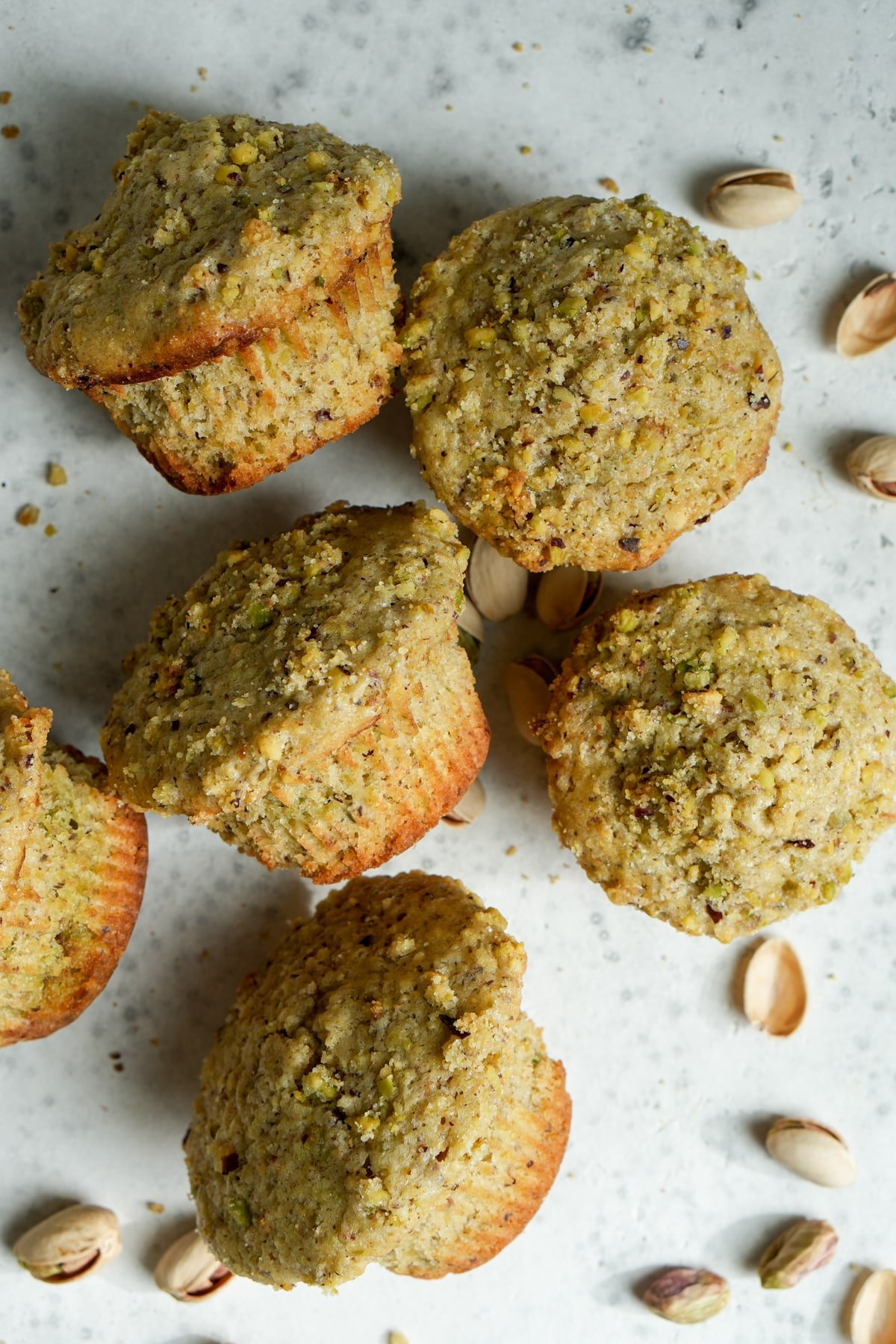 Overhead shot of five pistachio muffins surrounded by fresh pistachios in shell