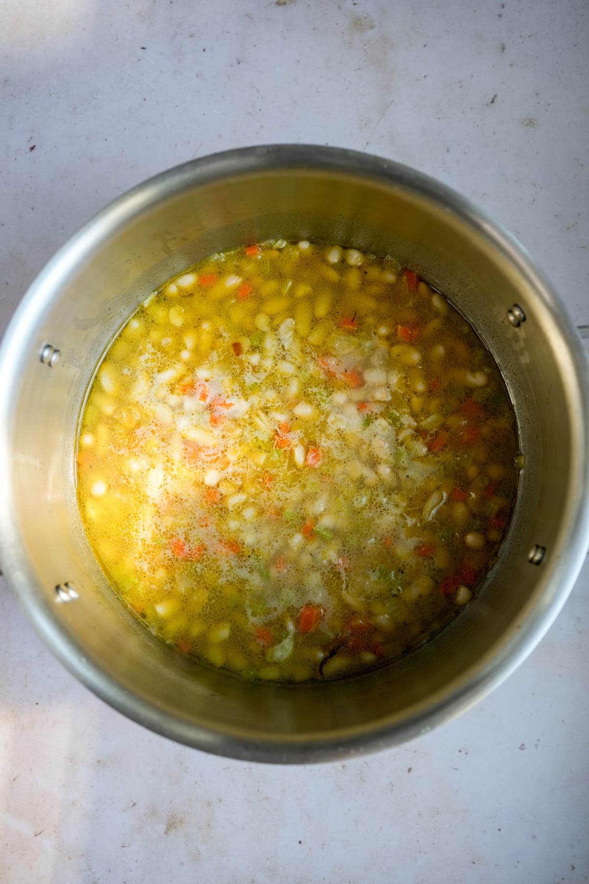 Italian white bean soup in a pot with whole white beans, chopped celery, carrot and onion