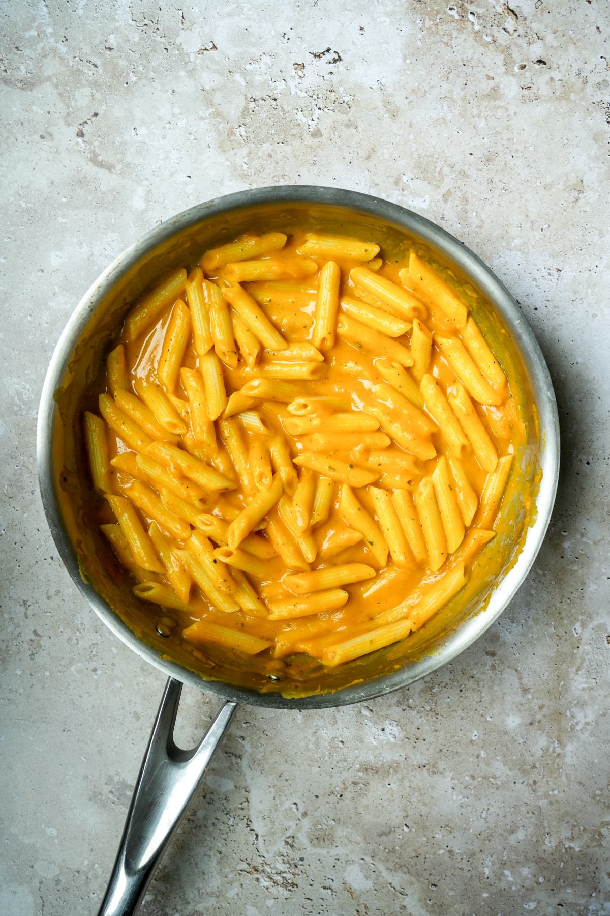 Penne pasta in a pan mixed with silky pumpkin pasta sauce