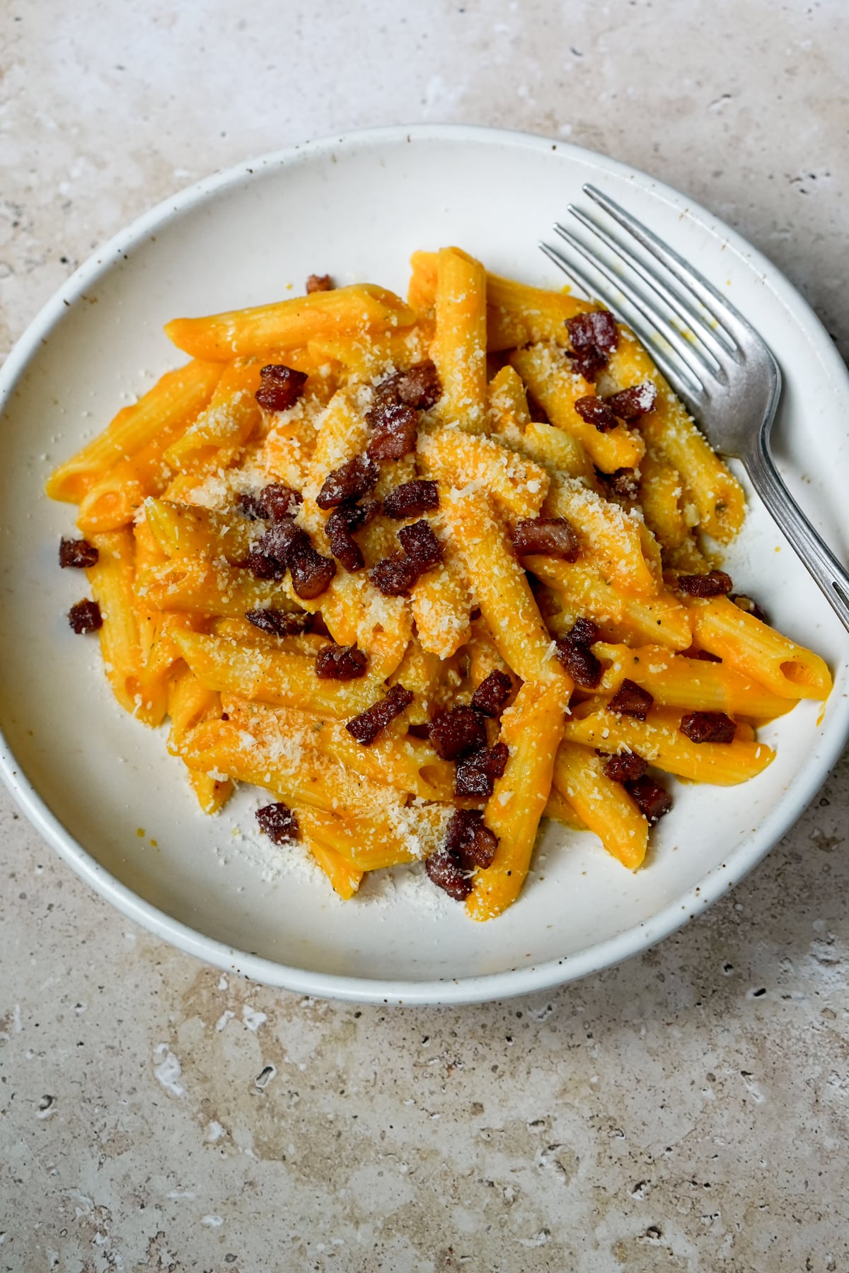 Bowl of penne with pumpkin pasta sauce with a fork to the side