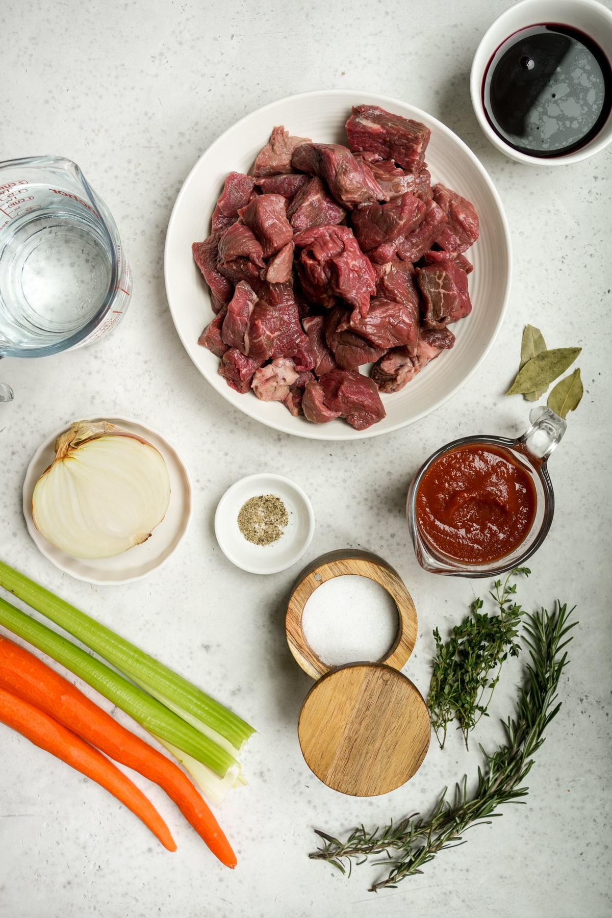 Italian beef stew (spezzatino) ingredients - cubed chuck roast, red wine, water, onion, carrot, celery, strained tomatoes, salt, pepper, bay leaves, fresh thyme and rosemary