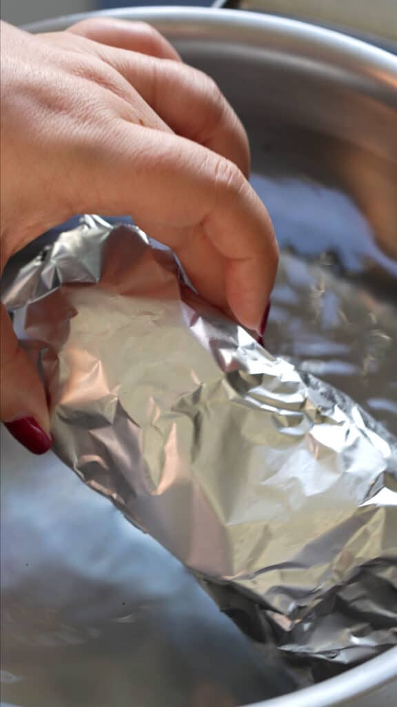 Cotechino wrapped in tin foil being submerged in water