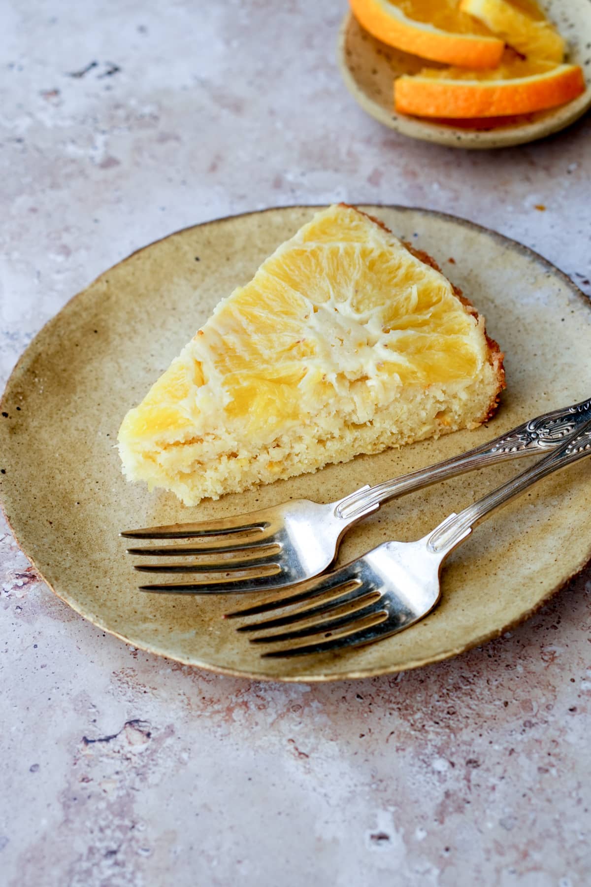 Slice of orange upside down cake in a plate with oranges in the background