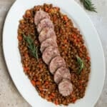 Cotechino in an oval platter on a bed of lentils garnished with rosemary