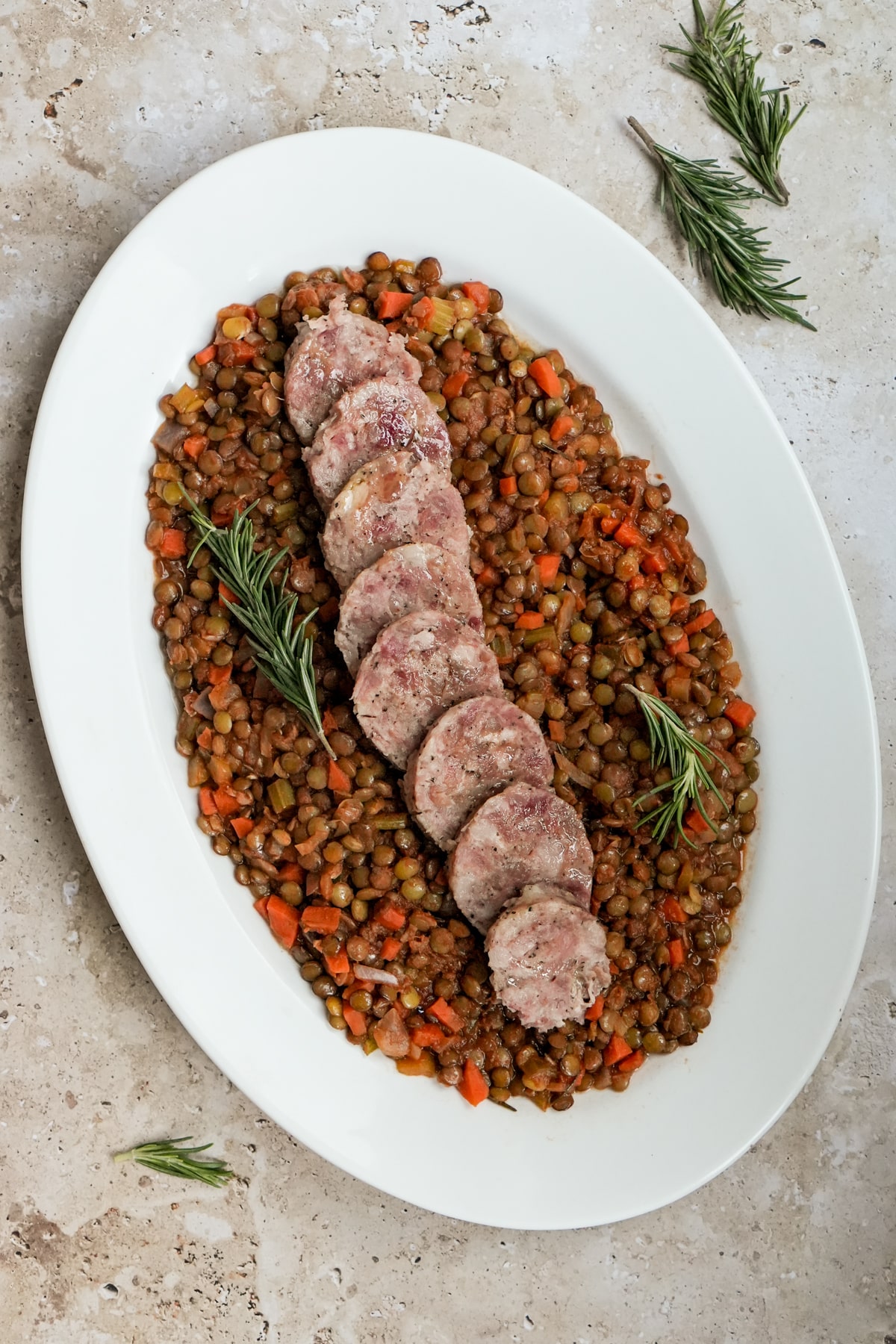Cotechino in an oval platter on a bed of lentils garnished with rosemary