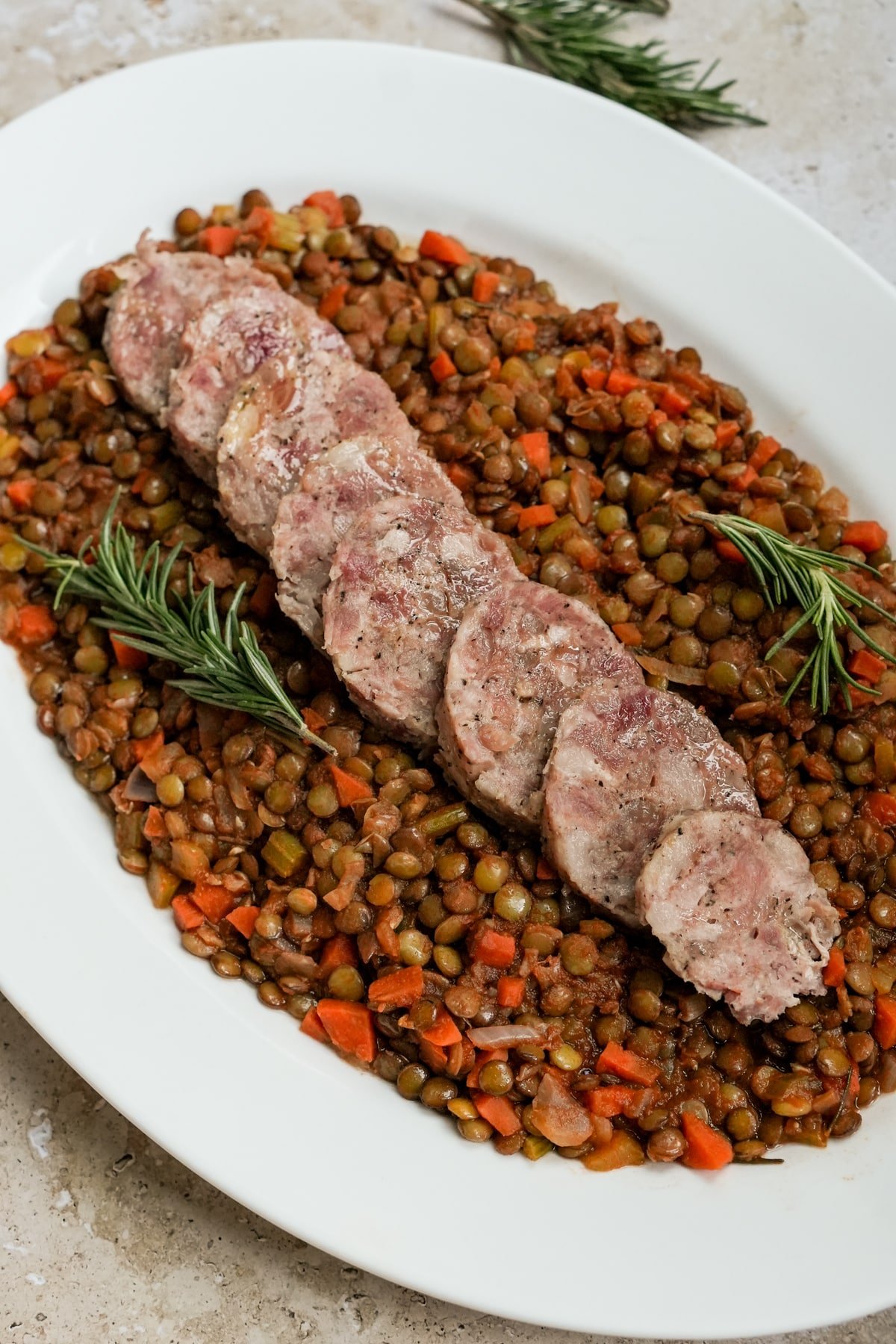 Sliced ccotechino in a platter on a bed of cooked lentils