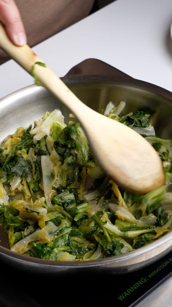 Escarole being sauteed in a pan with olive oil and garlic