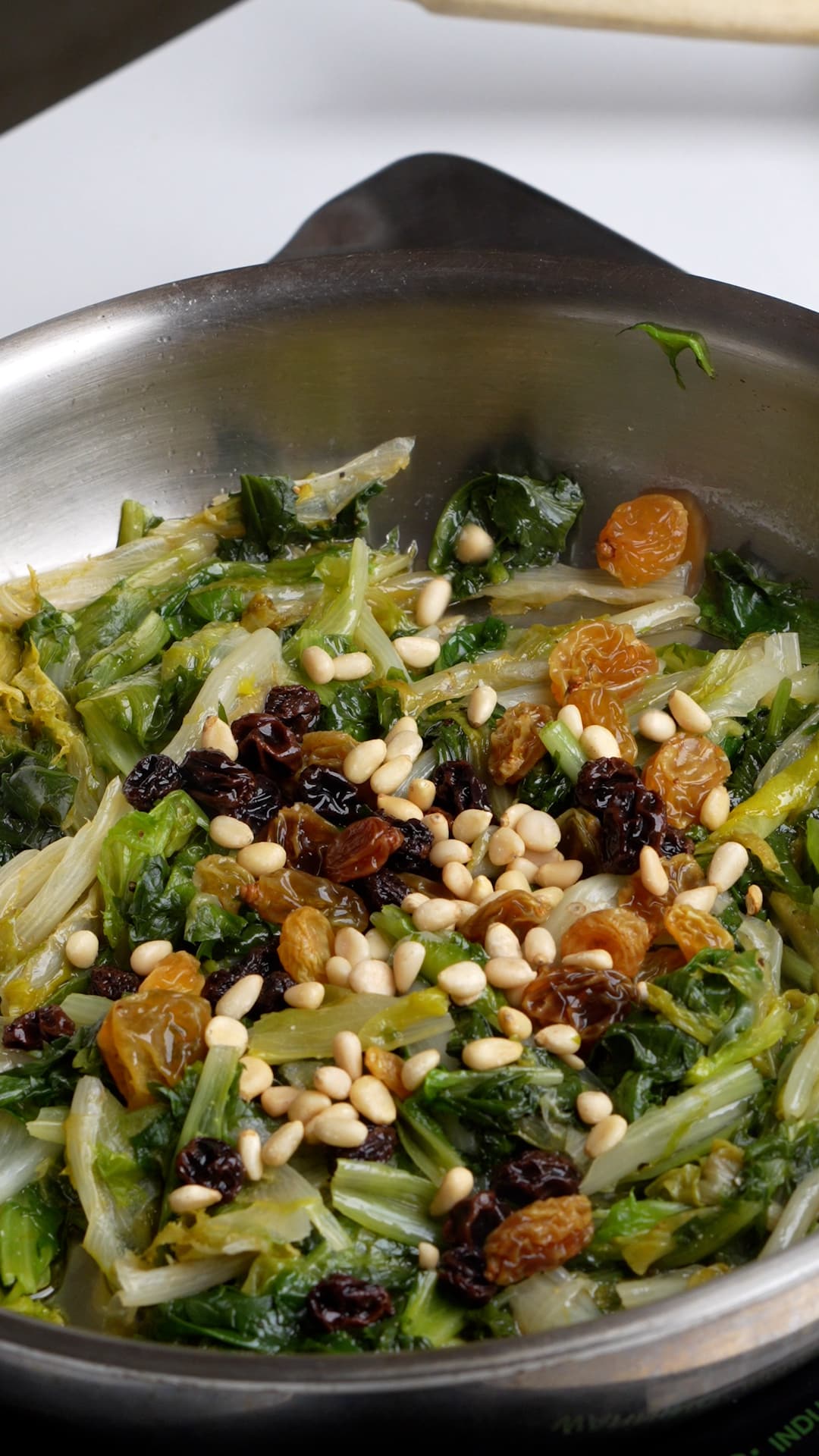Cooked endive in a pan with raisins and pine nuts
