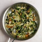 Overhead photo of cooked endive in a pan with raisins and pine nuts