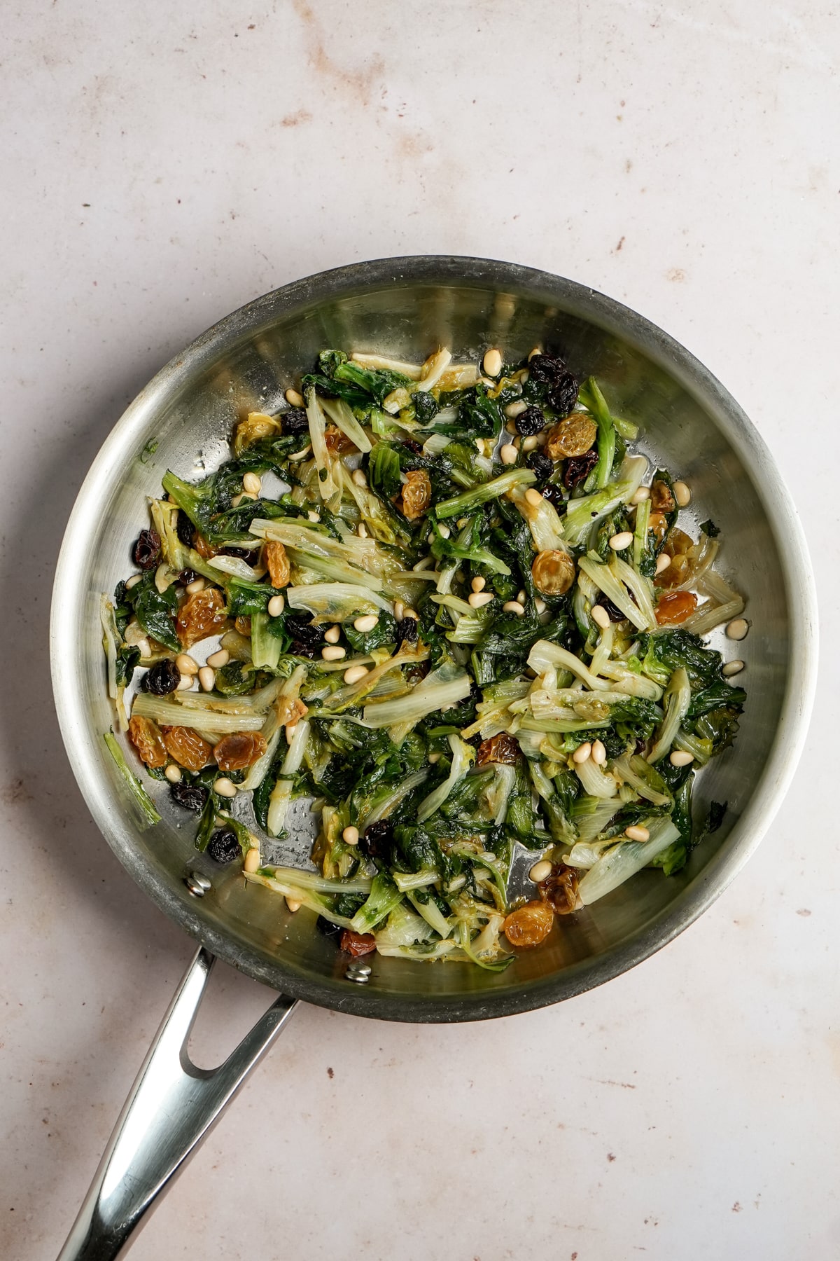 Overhead photo of cooked endive in a pan with raisins and pine nuts