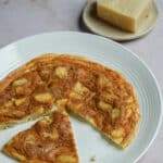 Potato frittata with a few pieces cut out and piece of parmigiano in the background