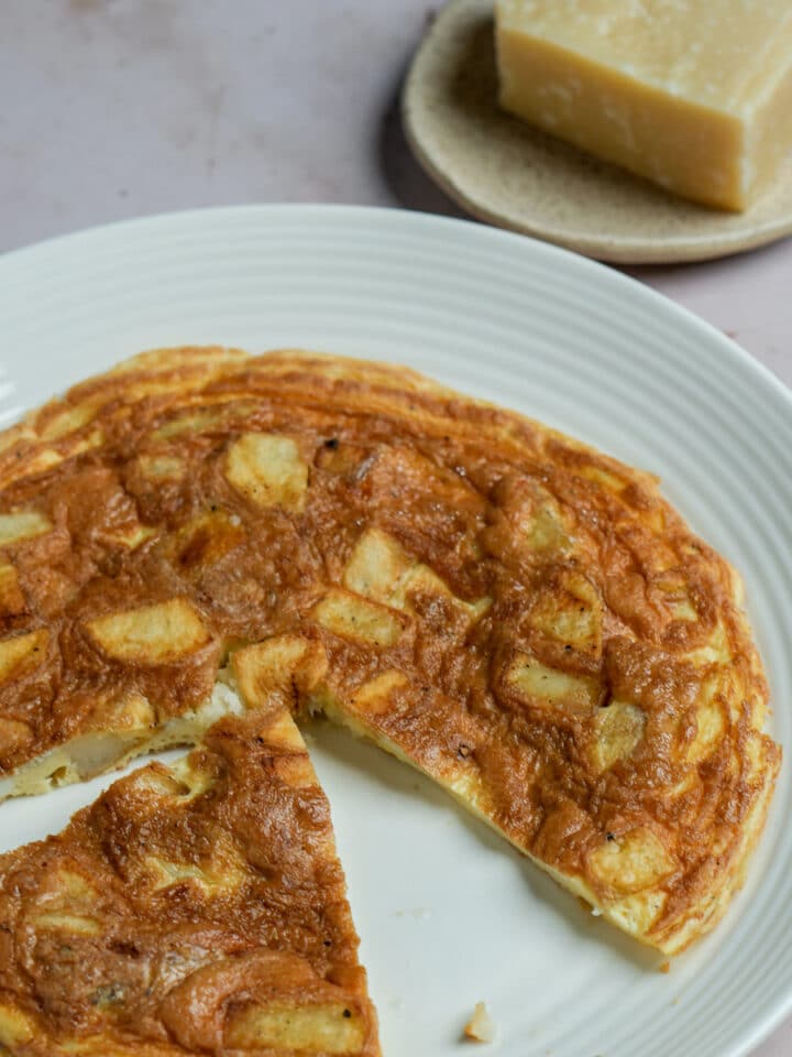 Potato frittata with a few pieces cut out and piece of parmigiano in the background