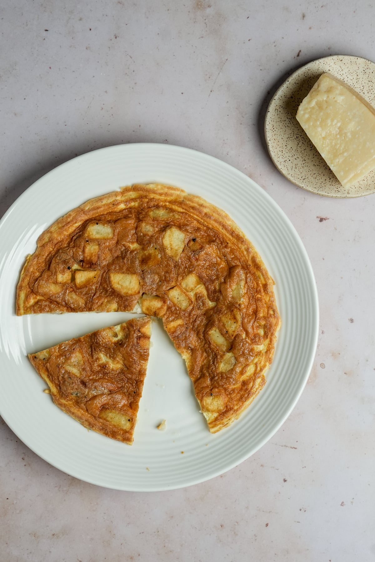 Potato frittata in a plate with a piece cut out with a block of parmigiano to the side