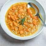Vegan barley soup in a bowl topped with a sprig of rosemary