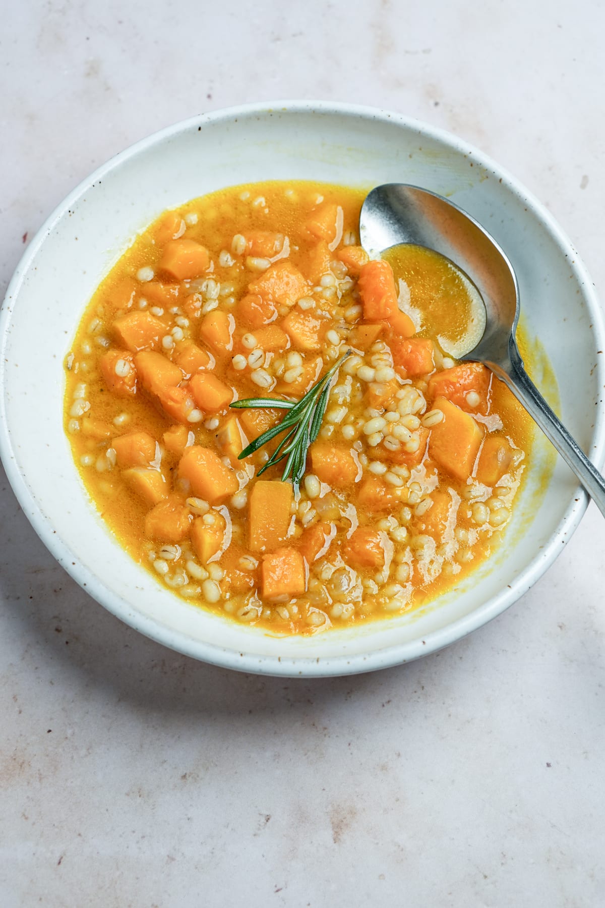 Vegan barley soup in a bowl topped with a sprig of rosemary
