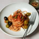 Pasta with tomato sauce, olives and capers in a bowl with a fork