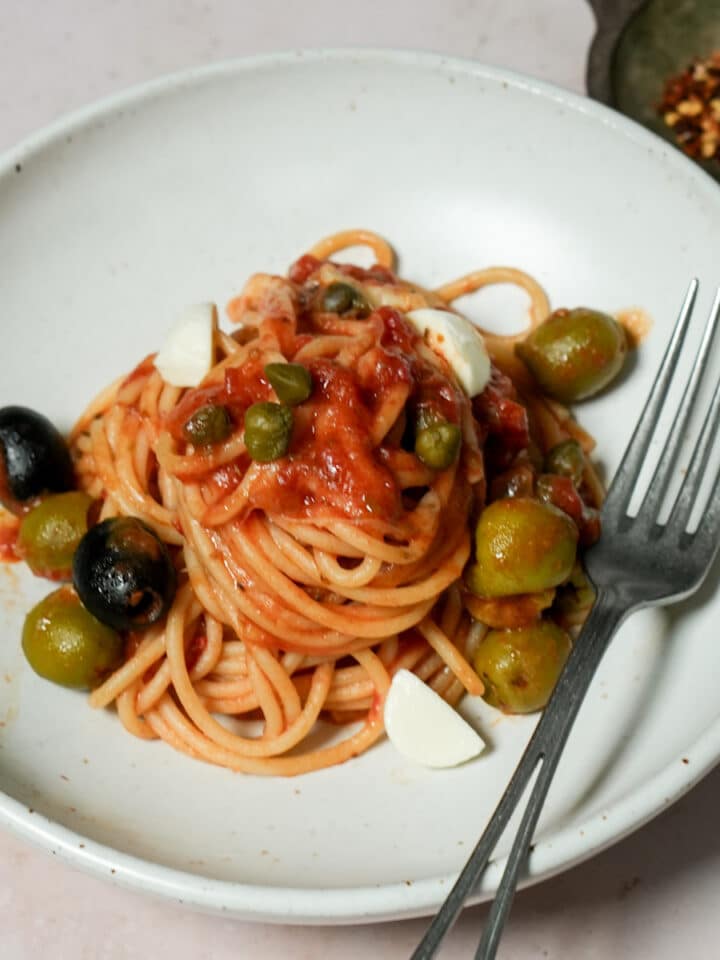 Pasta with tomato sauce, olives and capers in a bowl with a fork