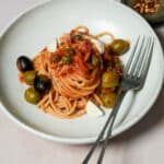 Vesuviana pasta in a dish with a fork, and small bowl of chili flakes in the background