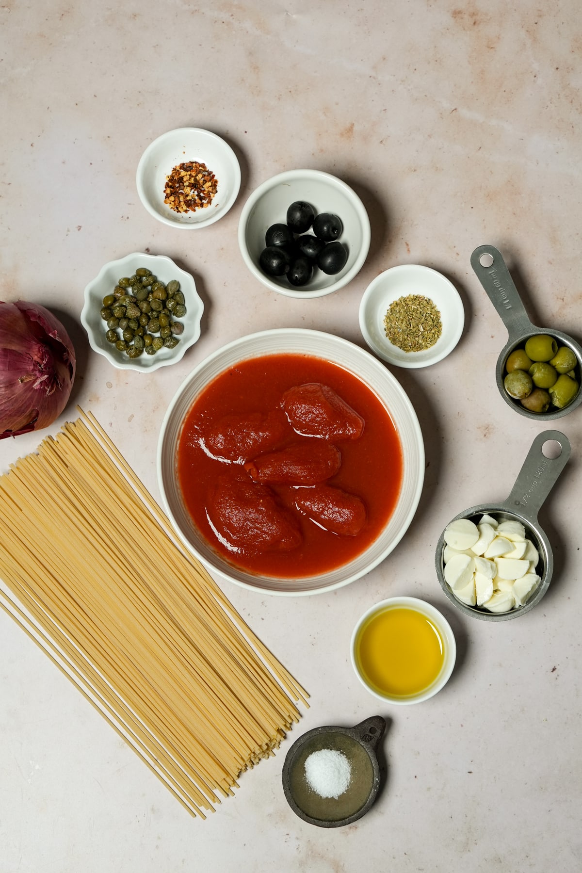 Vesuviana pasta ingredients - chili flakes, black olives, dried oregano, green olives, peeled tomatoes, mozzarella, olive oil, salt, spaghetti, red onion, capers