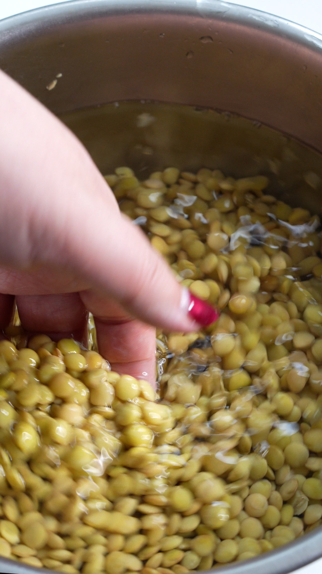 Dry lentils soaking in water with a hand gathering them