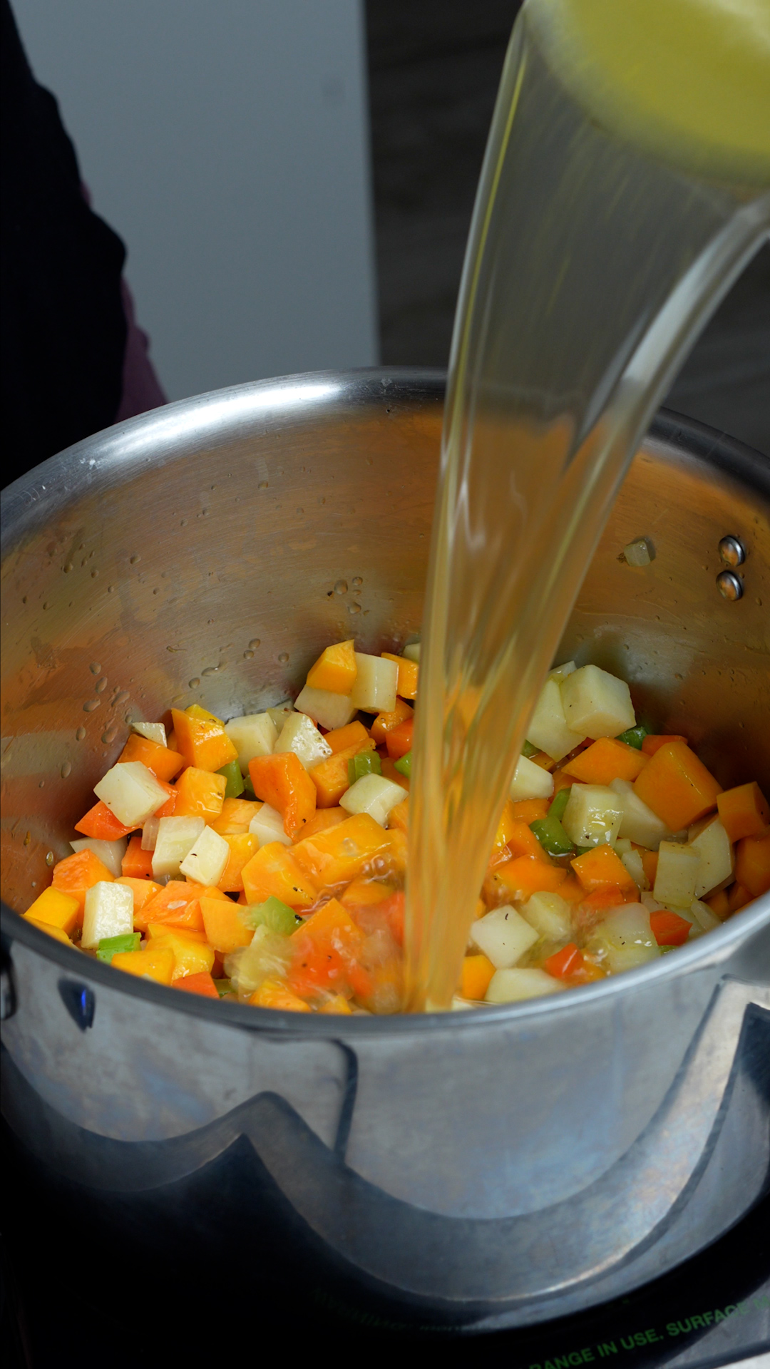 Step by step photos on how to make vegetarian rice soup - vegetable stock added to pot with celery, carrot, onion, potatoes and buttternut squash